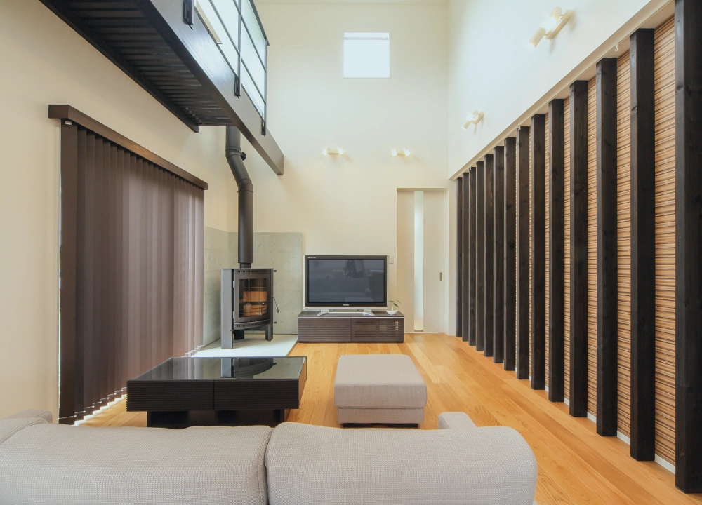 リビングの吹き抜け空間。黒いウッド調の柱と薪ストーブがモダンなデザインを引き立てる。